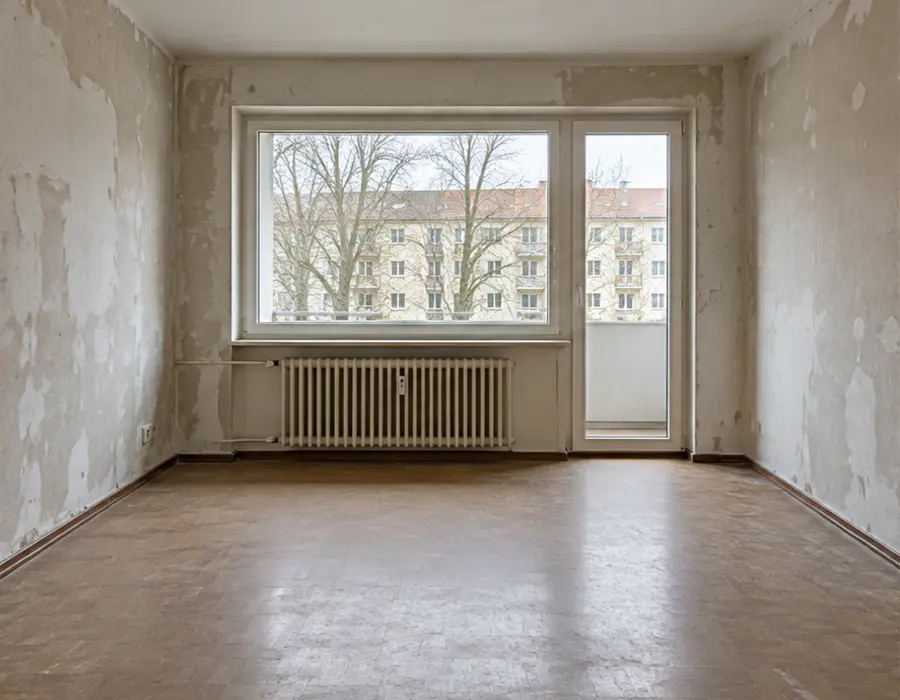 Wohnraum vor der Renovierung mit
sanierungsbedürftigen Wandflächen und altem Boden